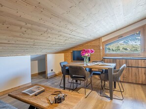 Una habitación acogedora con techo de madera, una mesa de comedor con sillas, un florero con flores y una ventana con vistas a la montaña.