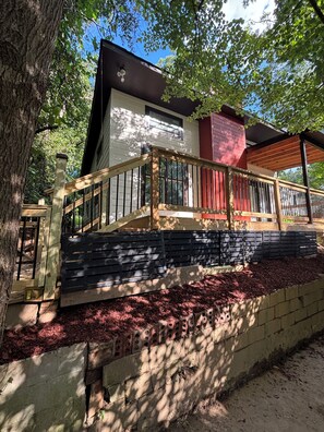 Ein zweistöckiges Haus mit einer Holzterrasse, einer Ziegelwand und einem Baum.