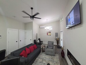 Ein Wohnzimmer mit einer Couch, einem Fernseher, einem Deckenventilator und einem Kamin.