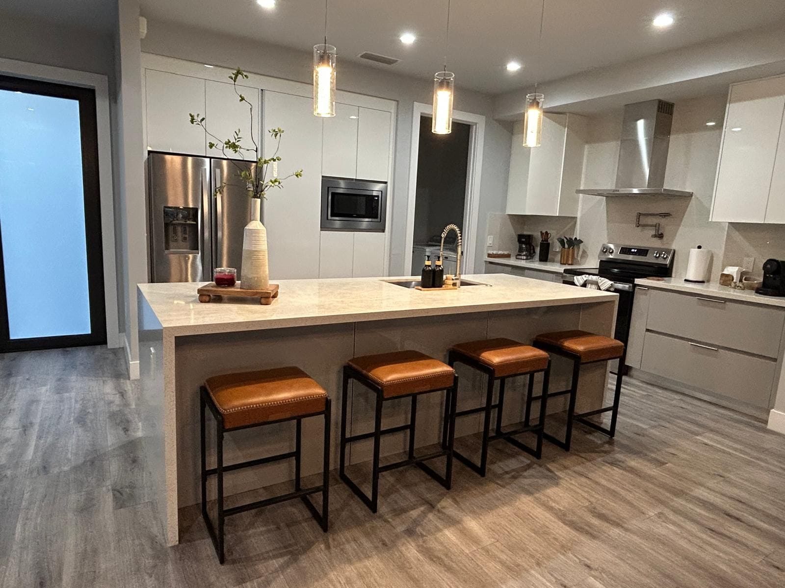 A modern kitchen with a central island, bar stools, stainless steel appliances, and pendant lighting.