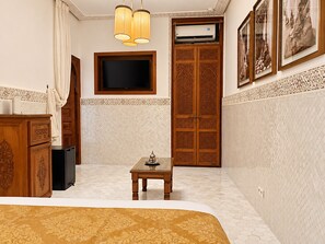 A hotel room with a bed, a TV, a table with a decorative item, a wardrobe, and a wall-mounted air conditioner. - Palais Tedya (Marrakech)