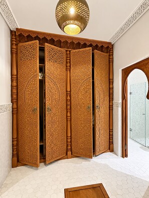 A room with a large, ornate wooden partition with intricate carvings, a ceiling light fixture, and a tiled floor. - Palais Tedya (Marrakech)