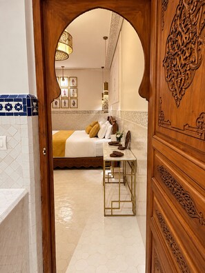 A hotel room with a bed, a desk, and a wooden door with intricate carvings. - Palais Tedya (Marrakech)