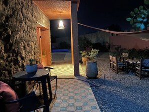 An outdoor patio area with a stone wall, a table with chairs, potted plants, and a hanging light fixture. - Vrbo Property (Lagfifat)