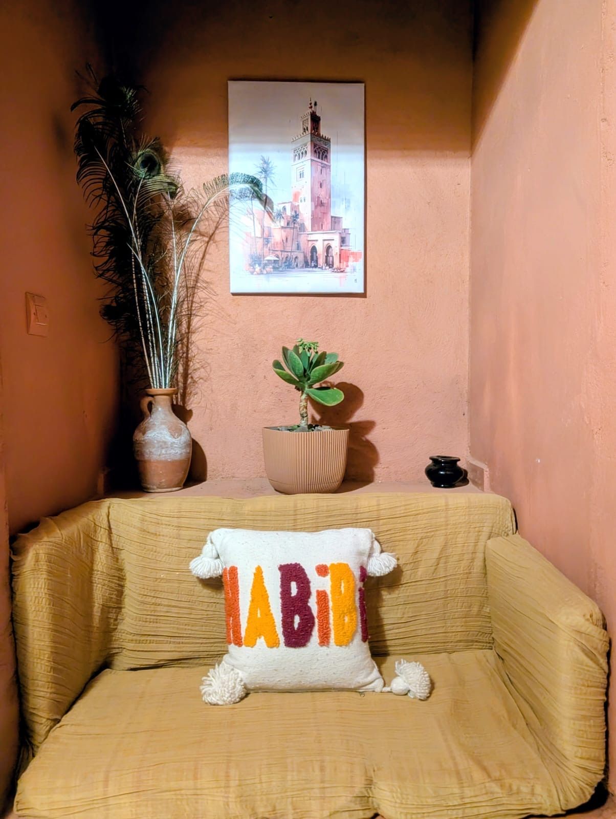 Ein Zimmer mit einem beigefarbenen Sofa, einem Kissen mit dem Schriftzug 'LADY', einer Topfpflanze und einem gerahmten Bild an der Wand.