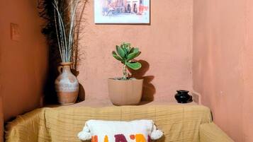 Ein Zimmer mit einem beigefarbenen Sofa, einem Kissen mit dem Schriftzug 'LADY', einer Topfpflanze und einem gerahmten Bild an der Wand.