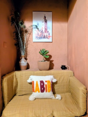 A room with a beige sofa, a cushion with 'LADY' text, a potted plant, and a framed picture on the wall.