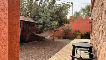 A patio area with a table and chairs, a hammock, and a garden with trees and a brick wall.