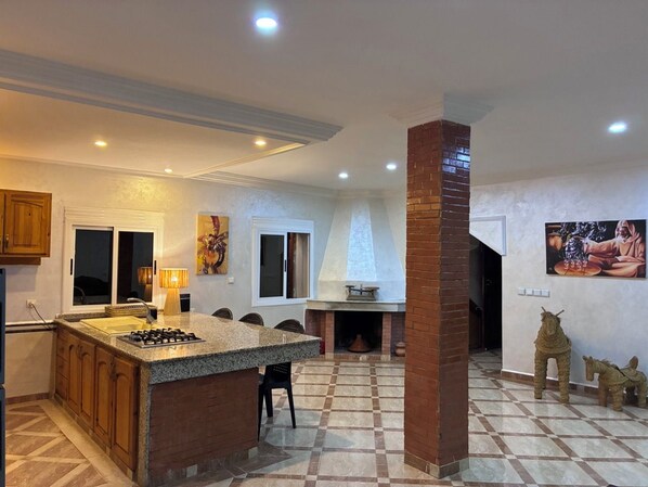 A kitchen with a central island, a fireplace, and a dining area with chairs.