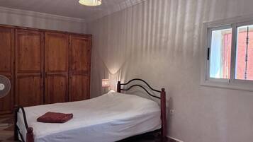 A bedroom with a bed, wooden wardrobe, and a window.