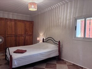 A bedroom with a bed, wooden wardrobe, and a window.