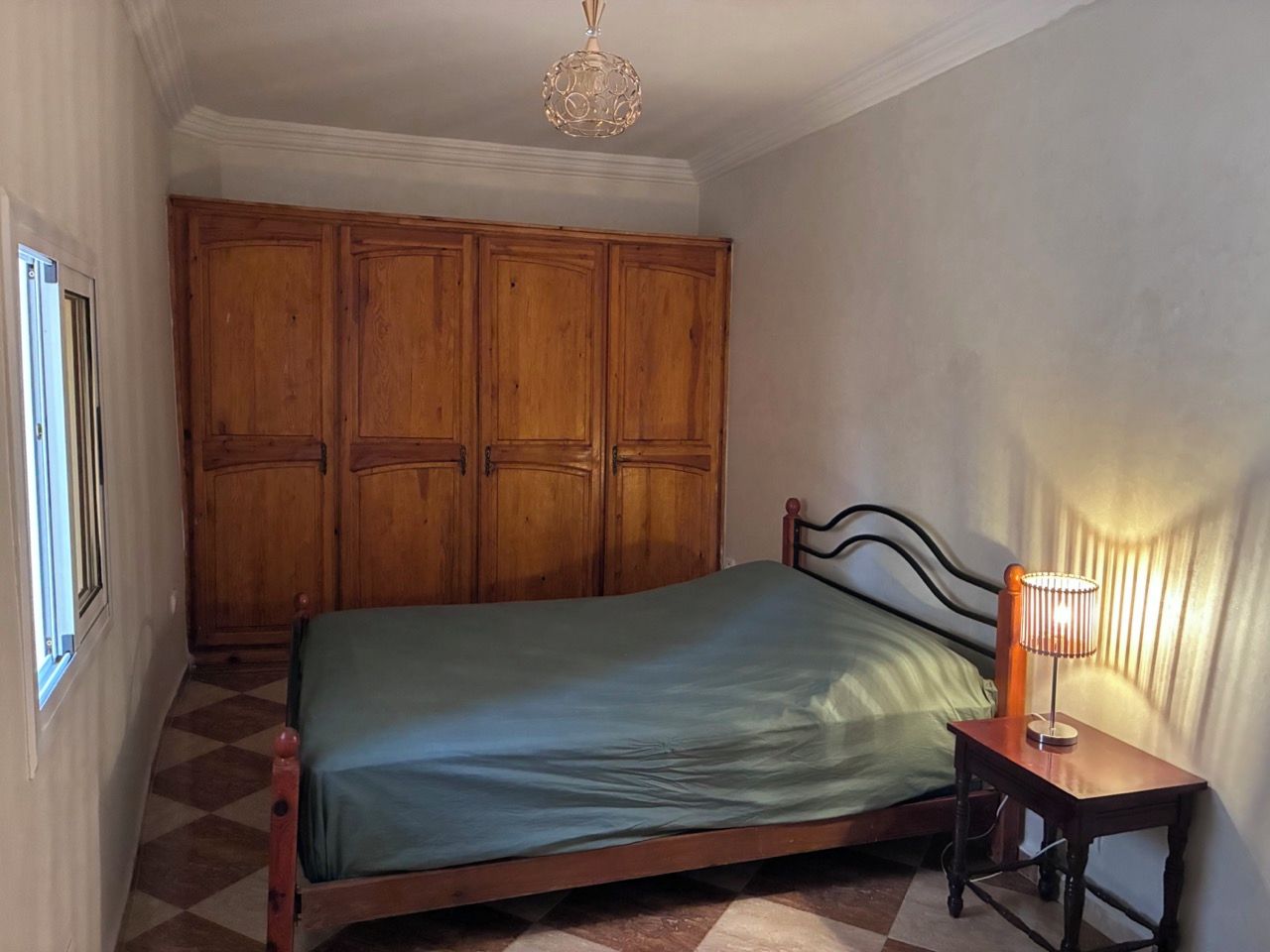 Une chambre à coucher avec un lit, une armoire en bois, une table de chevet avec une lampe et une fenêtre.