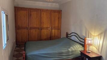 Une chambre à coucher avec un lit, une armoire en bois, une table de chevet avec une lampe et une fenêtre.