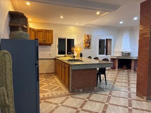 Una cuina amb una illa central, armaris de fusta, una cuina de foc integrada i una llar de pedra.