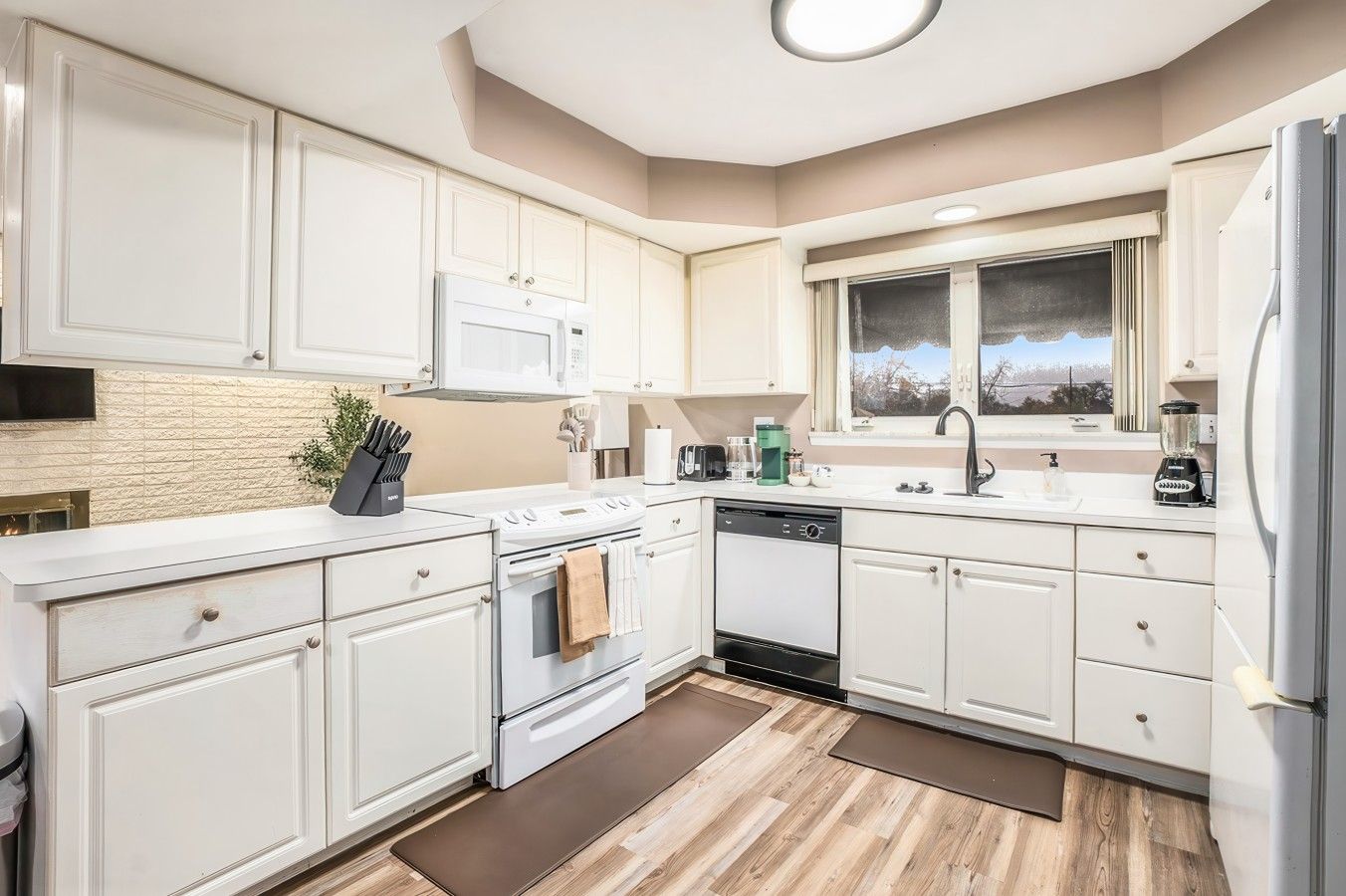 A modern kitchen with white cabinetry, a built-in oven, a dishwasher, and a window with a view.