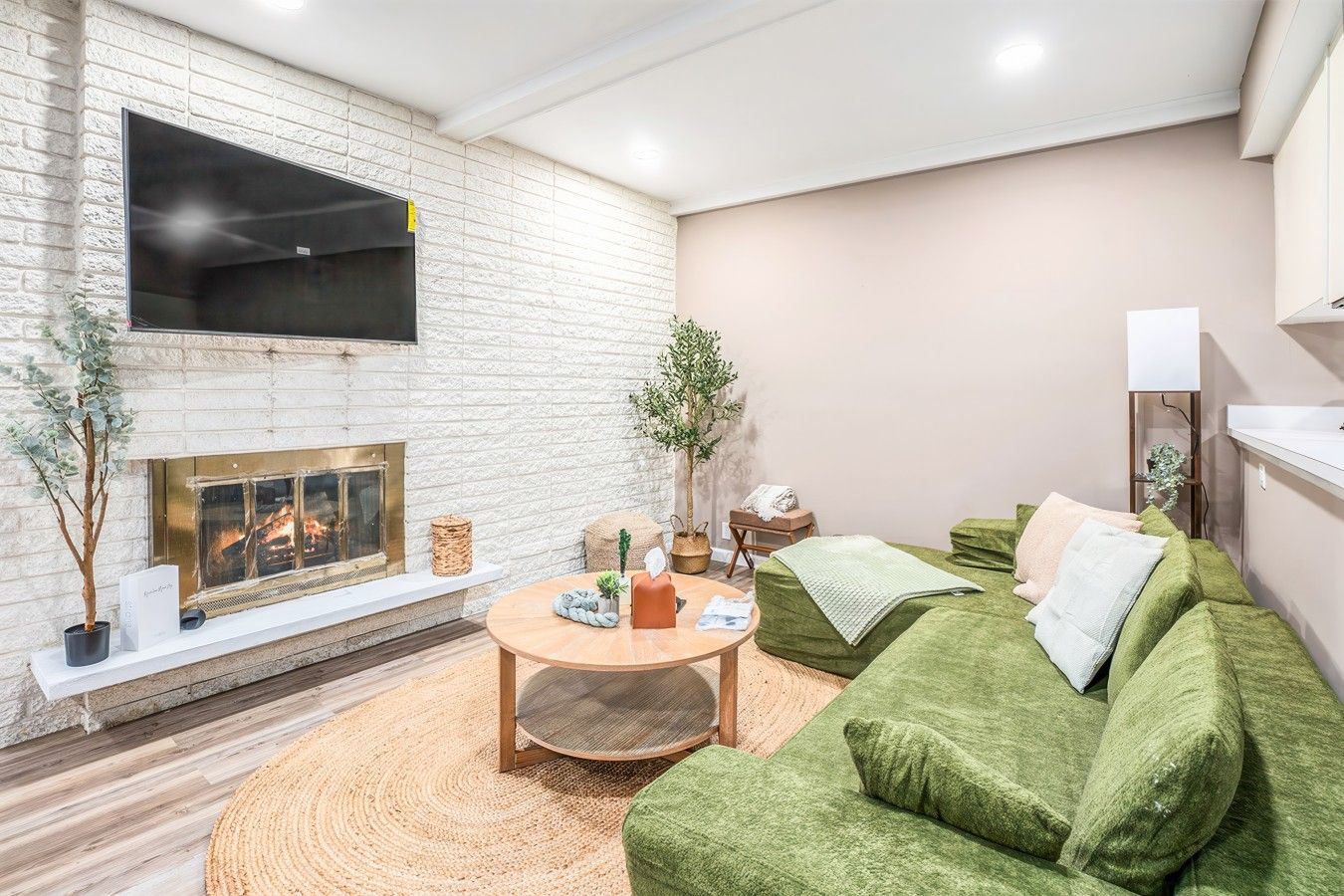 Una sala de estar con chimenea, un sofá verde, una mesa de centro redonda y un televisor montado en la pared.