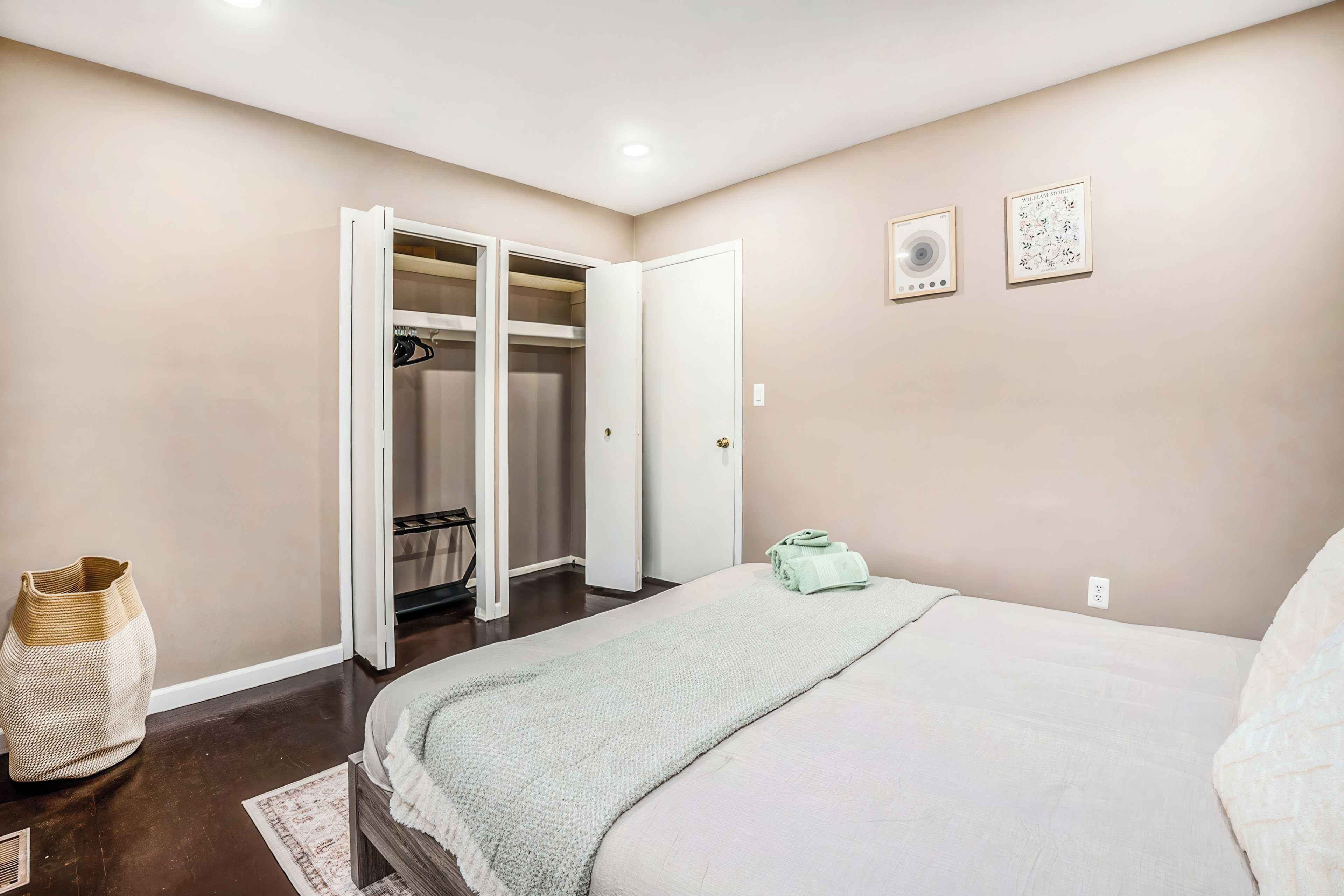 A bedroom with a bed, a closet with open doors, a woven basket, and two framed pictures on the wall.