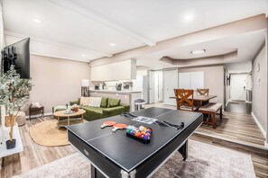 Un espacio moderno para vivir con mesa de ping pong, sofá, mesa de comedor y zona de cocina.
