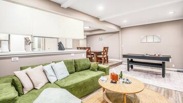 A modern living room with a green sofa, a round coffee table, and a pool table.