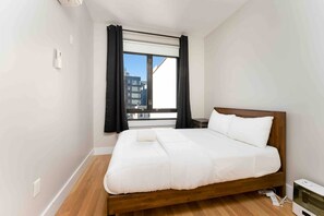 Un dormitorio con una cama de madera, una ventana con cortinas, una mesita de noche y un aire acondicionado instalado en la pared.