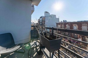 A balcony with a chair, a potted plant, and a view of buildings. - Prime Greenpoint 3BR • Balcony • Park View (Brooklyn)