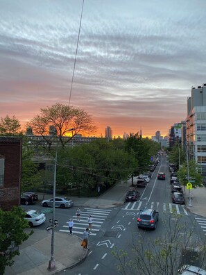 Una calle urbana al atardecer con edificios, coches y peatones.