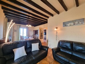 A living room with two black leather sofas, a dining area with a table and chairs, and a kitchen in the background. - Comfortable house, pets allowed - 6 guests (SAINT CYPRIEN)