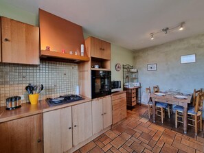 A kitchen with wooden cabinets, a gas stove, an oven, and a dining area with a table and chairs. - Comfortable house, pets allowed - 6 guests (SAINT CYPRIEN)