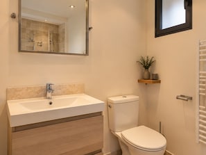 Ein Badezimmer mit einem Doppelwaschtisch, einer Toilette, einem Spiegel und einem Regal mit einer Pflanze.
