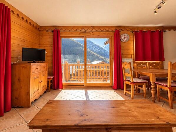 A wooden interior with a dining table, chairs, a television on a cabinet, and a view of mountains through a glass door. - Charming apartment, parking - 6 guests (Champagny-en-Vanoise)