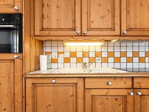 A kitchen with wooden cabinets, a stainless steel oven, a tiled backsplash, and a sink with a faucet. - Charming apartment, parking - 6 guests (Champagny-en-Vanoise)