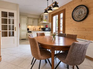Ein Essbereich mit Holztisch und -stühlen, eine Küche im Hintergrund und eine Holzwand mit einer Uhr.