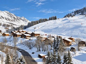 Ein verschneites Bergdorf mit Holzhäusern, einer Skipiste und einem klaren Himmel.
