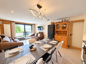 A modern living room with a dining area, wooden cabinets, and a flat-screen TV. - Ideally located apartment - 6 guests (Les Gets)
