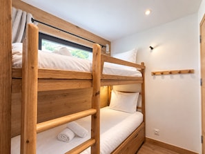 Ein Stockbett mit Holzrahmen, ein Fenster mit Vorhängen und ein an der Wand befestigter Kleiderhaken.