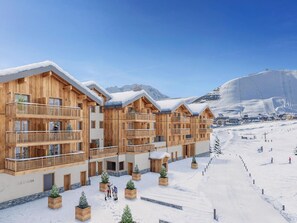 A wooden chalet-style hotel with balconies, set against a snowy mountain backdrop. - Ideal apartment at the slopes - 6 guests (Huez)