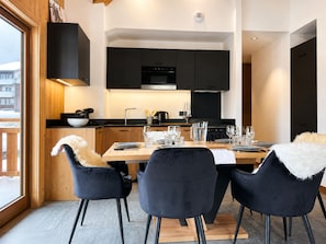 A modern kitchen with black cabinets, a wooden dining table set for four, and a large window on one side. - Ideal apartment at the slopes - 6 guests (Huez)