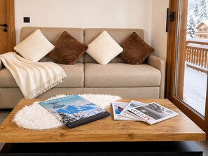 A cozy living room with a sofa, pillows, a white fluffy rug, and a wooden coffee table with books and magazines. - Ideal apartment at the slopes - 6 guests (Huez)