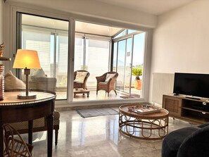 Un soggiorno moderno con televisione, mobili in vimini e vista attraverso ampie vetrate.