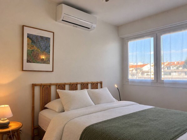 Una camera da letto con un letto, un condizionatore, una finestra vista e una lampada su un comodino.