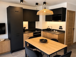 Una cocina moderna con armarios oscuros, una mesa de comedor de madera y una lámpara colgante.
