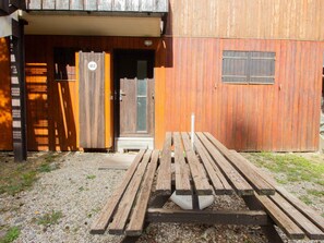 Ein Holzgebäude mit Tür und Fenster, einer Bank und einem Kiesweg.