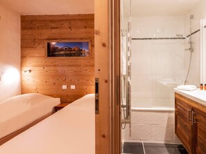 A wooden-paneled room with a bed, a bathroom with a shower, and a picture on the wall. - Comfortable apartment with slope view - 6 guests (Val-d'Isère)