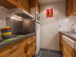 A compact kitchen with wooden cabinets, a stainless steel range hood, a microwave, and a sink. - Comfortable apartment with slope view - 6 guests (Val-d'Isère)