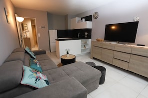 Ein modernes Wohnzimmer mit einem grauen Ecksofa, einem Flachbildfernseher und einer minimalistischen Küchenzeile.