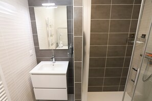 Ein Badezimmer mit einem weißen Waschbecken, einem Spiegel und einer Duschkabine mit dunklen Fliesen.