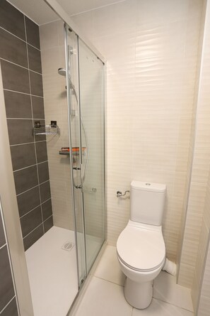 A bathroom with a glass-enclosed shower, a toilet, and a shelf with toiletries. - St Cyprien Terrace apartment 2 minutes from the port and the beach (Saint-Cyprien)