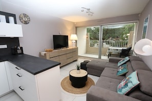 A modern living room with a sofa, a coffee table, a TV, and a balcony with a view of trees. - St Cyprien Terrace apartment 2 minutes from the port and the beach (Saint-Cyprien)