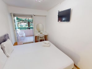 Ein Hotelzimmer mit Bett, Schreibtisch, Stuhl, Fernseher und einem Balkon mit Sitzgelegenheiten.