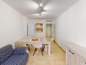 Ein modernes Wohnzimmer mit einer Couch, einem Esstisch mit Stühlen, einer Küchenzeile mit Schränken und einer Deckenleuchte.